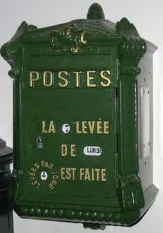 a green post box mounted to the side of a wall