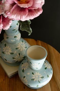 a blue vase with pink flowers in it sitting on a wooden table next to a book