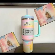 a pink and blue tumbler next to two pictures on a table with the lid open