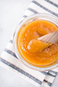 a wooden spoon sitting in a glass bowl filled with orange marmalade sauce on top of a striped napkin