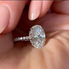 a woman's hand holding an oval diamond ring with diamonds on the band and side