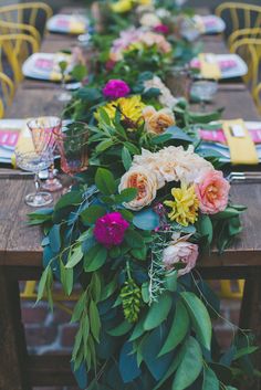 a long wooden table topped with lots of flowers and greenery on top of it