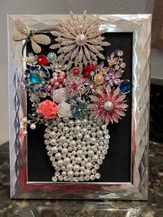 an art piece with flowers and pearls in it on a table top next to a wall