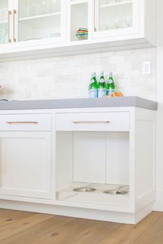 a kitchen with white cabinets and wood flooring is pictured in this image, there are bottles on the counter