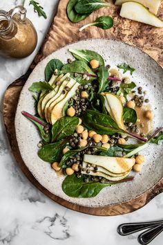 a white plate topped with spinach, pears and other vegetables on top of a wooden cutting board