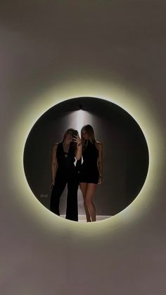 two women standing in front of a circular light with one woman taking a selfie