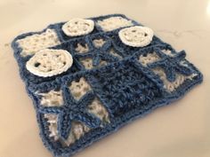 a crocheted blue and white square with buttons on it sitting on a table