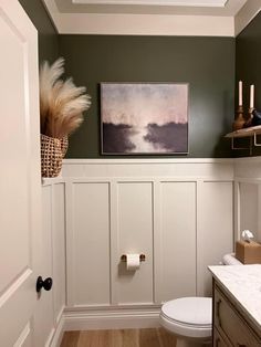 a white toilet sitting in a bathroom next to a wooden cabinet under a painting on the wall