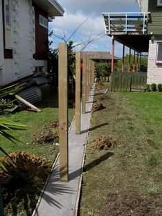 a wooden fence in front of a house with grass on the ground and bushes growing next to it