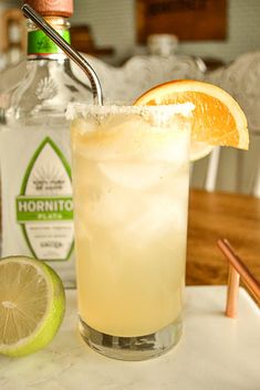 a drink with an orange slice on the rim and a bottle in the back ground