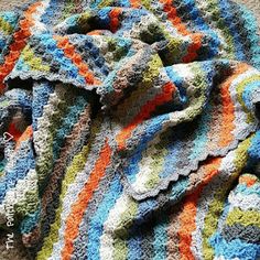 a crocheted blanket is laying on top of a tablecloth that has been made with multicolored yarns