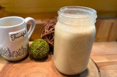 a jar of milk next to a mug on a wooden table with moss and twine