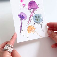 a person holding up a card with watercolor drawings on it