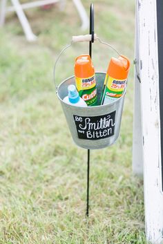 a metal bucket with bottles in it on top of a grass covered field next to a white fence