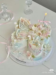 a cake decorated with flowers and butterflies on a table next to two wine glass holders