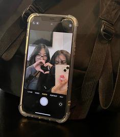 a cell phone sitting on top of a brown bag next to a handbag and another person taking a photo