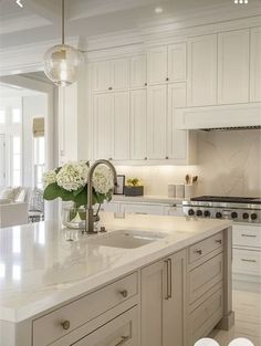 a white kitchen with marble counter tops and an island in front of the stove top