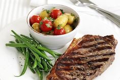 a white plate topped with steak and green beans next to a bowl of potato salad