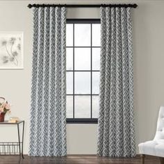 a living room with a chair and window covered in gray patterned drapes next to a table