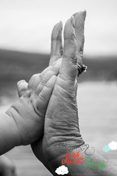 an older person holding their baby's hand up to the sky with water in the background