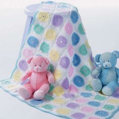 two teddy bears are sitting next to a crocheted blanket