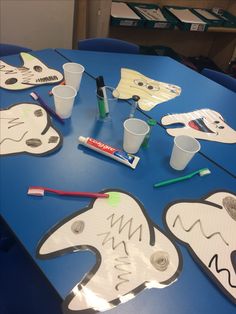 a blue table topped with paper cutouts and cups filled with toothbrushes on top of it