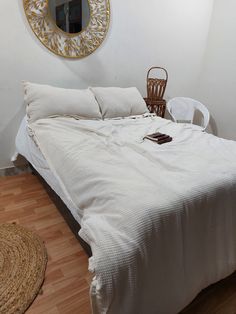 a white bed sitting in a bedroom next to a wooden floor and a round mirror on the wall