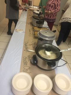 there are many bowls on the table with soup in them and people standing around it