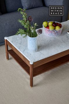 a marble coffee table with flowers and fruit on it in front of a gray couch