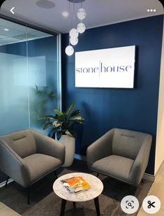 two gray chairs sitting next to each other in front of a blue wall with the stone house logo on it