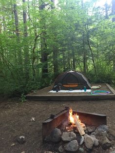 a campfire in the middle of a forest with a tent set up next to it