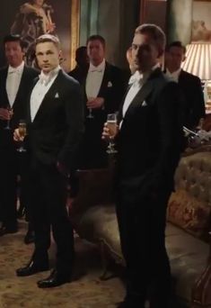 a group of men in tuxedos standing next to each other holding wine glasses