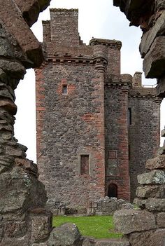 an old brick castle with stone walls and grass in the foreground, through which is a doorway that leads to another building