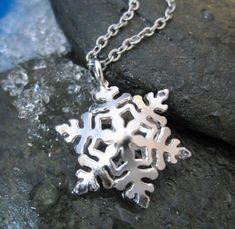 a silver snowflake necklace sitting on top of a rock