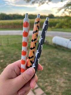 two pens with halloween designs on them are held up in front of a grassy area