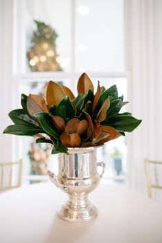 a silver vase filled with flowers on top of a white table next to a window