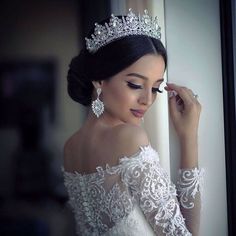 a woman wearing a tiara and holding her hair in one hand while looking out the window