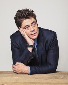 a man in a suit sitting at a table with his hand on his chin and looking off to the side