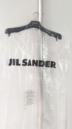 a plastic bag hanging on the wall with a hanger attached to it that says jil sander