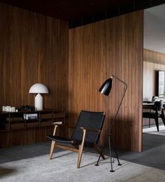 a black chair sitting in front of a wooden wall with a lamp on top of it