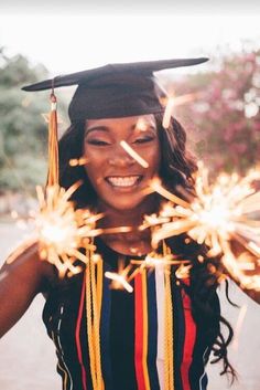 a woman in graduation cap and gown holding sparklers