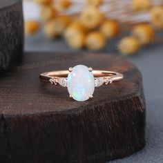 a white opal and diamond ring sitting on top of a wooden table next to other items