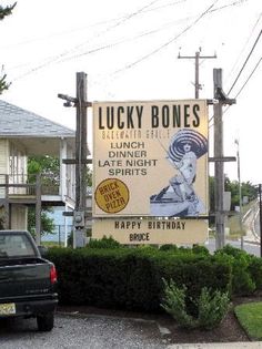 a sign for lucky bones sits in front of a car parked on the side of the road