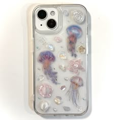 an iphone case with jellyfishs and seashells on the back, sitting on a white surface