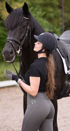 a woman standing next to a black horse with a saddle on it's back