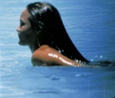 a woman is swimming in the water with her long hair blowing back and looking off into the distance