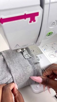 two hands are working on a sewing machine with pink thread and scissors in front of it