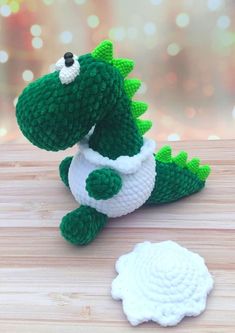 a crocheted green and white toy sitting on top of a wooden table next to a paper plate