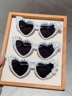 four pairs of black and white heart shaped sunglasses in a wooden frame with pearls on the sides