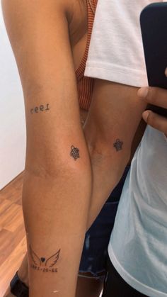 two people standing next to each other with tattoos on their arms and legs, one holding a cell phone